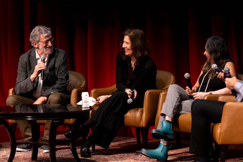 Three people sitting in tan armchairs on stage at the summit, holding microphones.