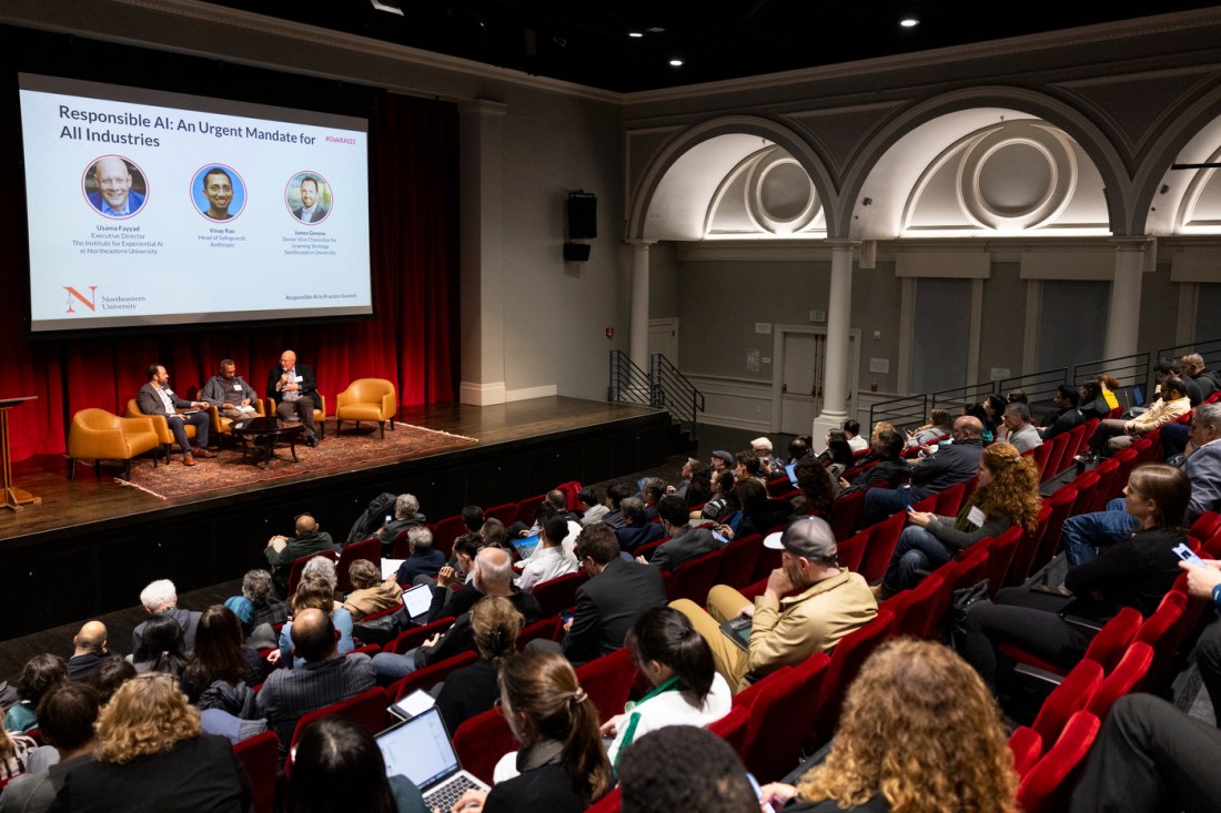 James Genone, Vinay S. Rao, and Usama Fayyad sitting in tan leather chairs at the front of an auditorium filled with audience members. Above them is a projector screen displaying portraits and brief bios of each of them. The title of the slide is 'Responsible AI: An Urgent Mandate for All Industries'.