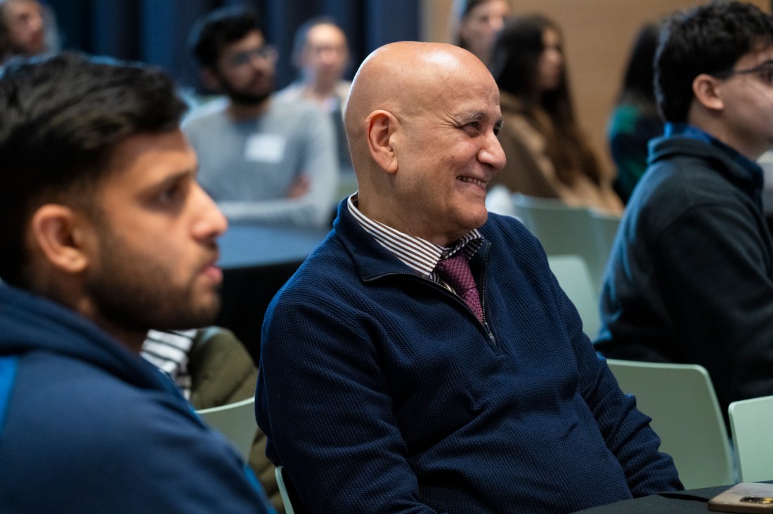 An audience member wearing a tie and button down under a quarter zip smiling. 