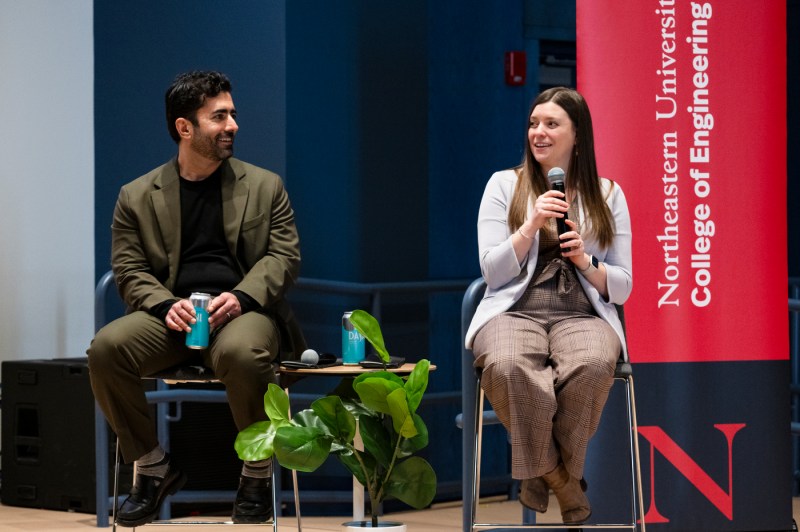 Emily Wisniewski  holding a microphone sitting on stage next to Hamed Tabkhi.