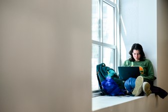 A person sits by a window with a laptop, focused on their work, in a quiet space.