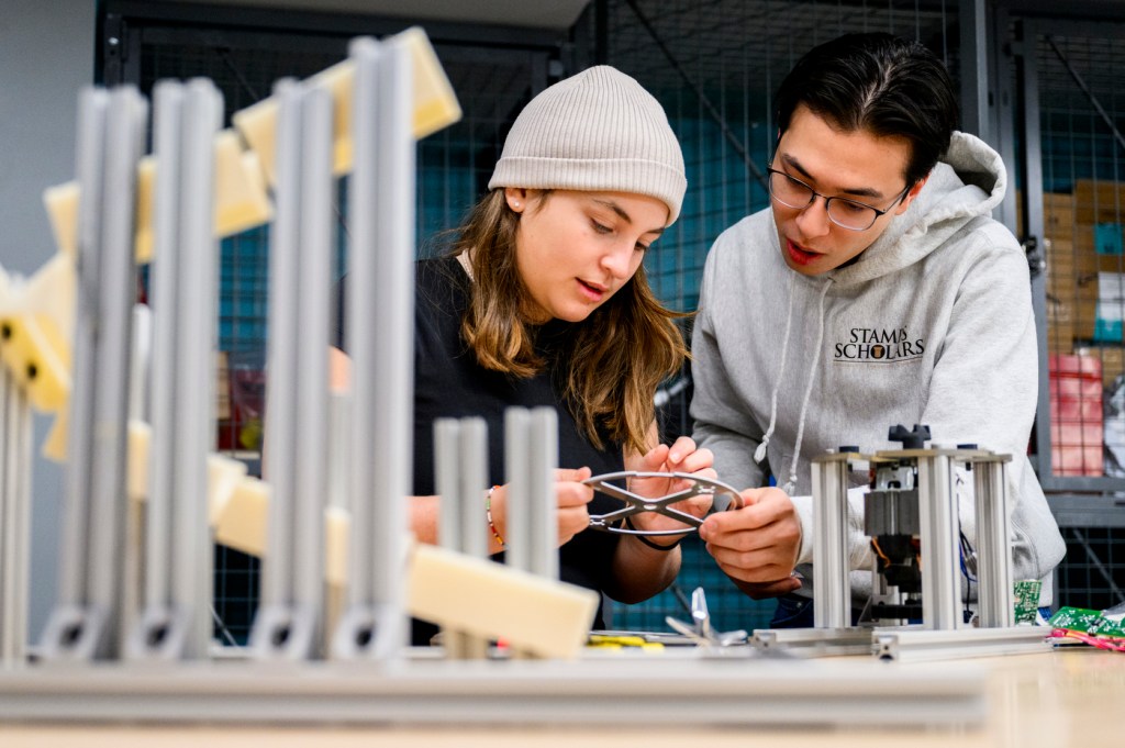 Two people collaborate on a hands-on project, focusing on assembling a mechanical structure in a workshop setting.