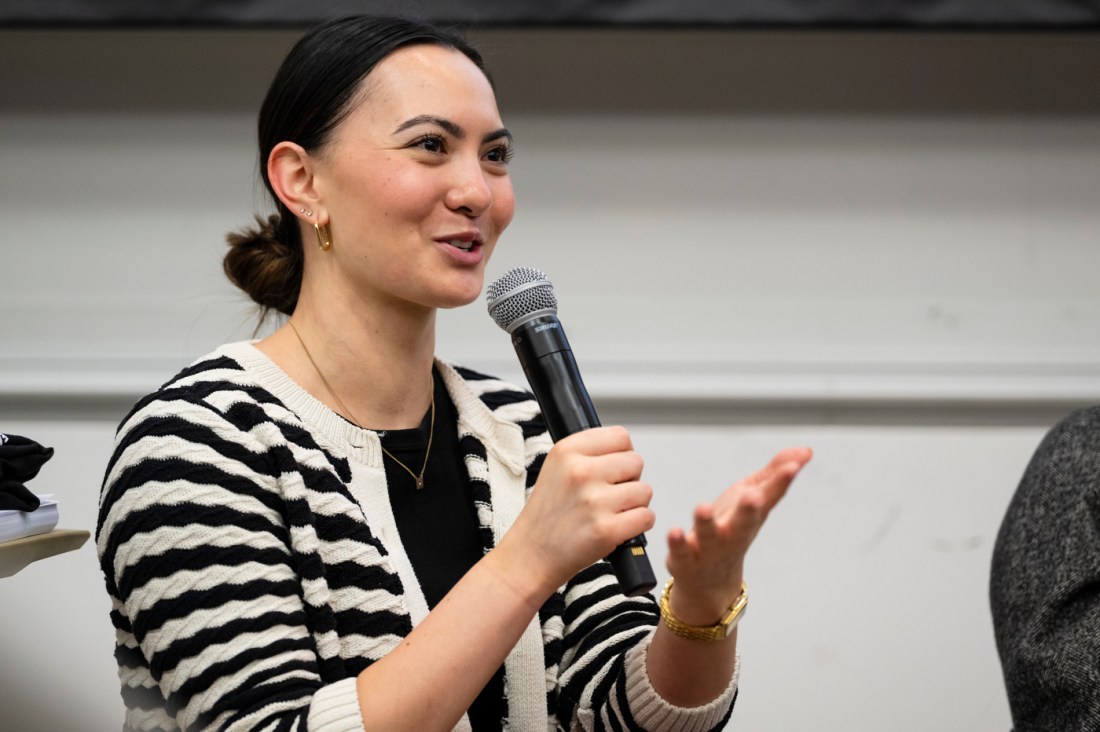 A speaker wearing a cardigan holding a microphone at a panel discussion. 