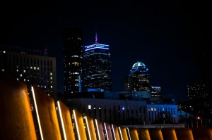 A city skyline at night with illuminated buildings and lights in the foreground.