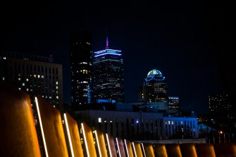 A city skyline at night with illuminated buildings and lights in the foreground.