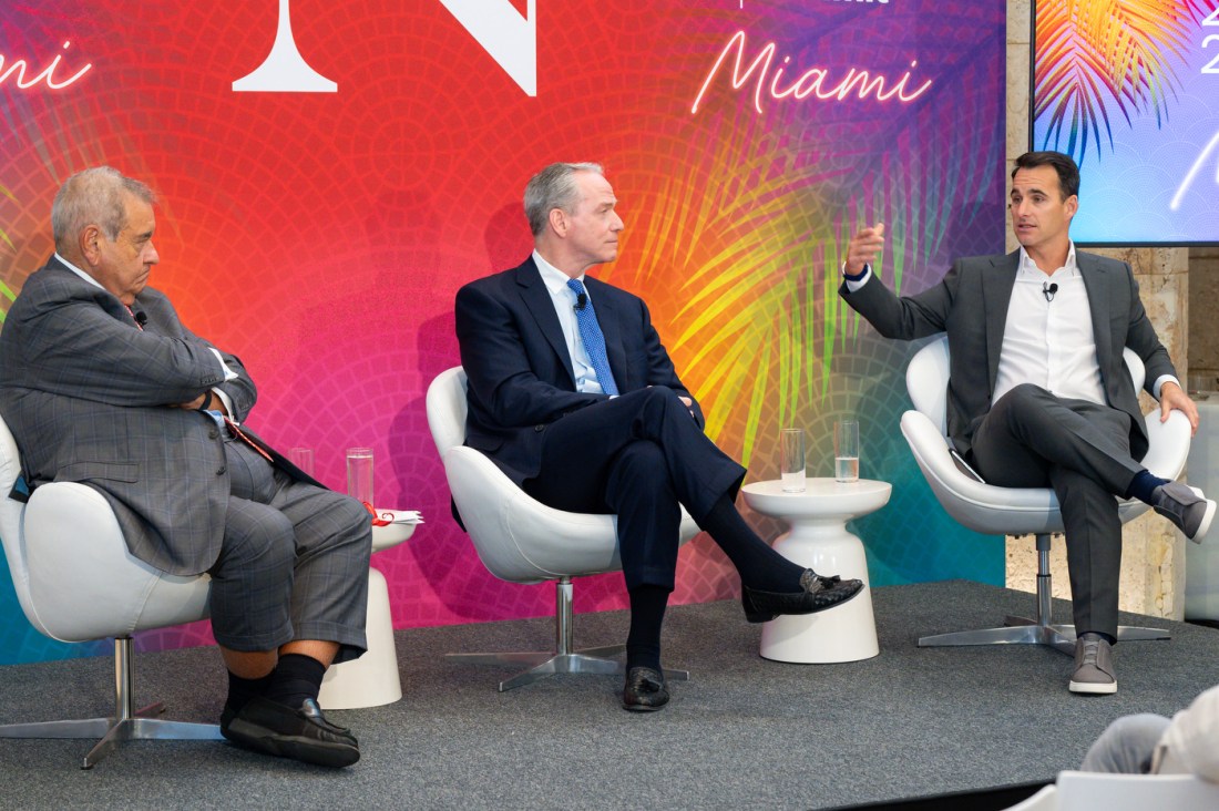 Three people sitting in white swivel chairs on stage in a building at the Global Leadership Summit in Miami.