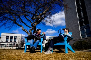 People enjoy the outdoors on a sunny day near a campus building.
