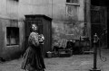 A black and white screen capture from The Girl with the Needle. It shows a girl in an alley way looking up and over her shoulder as if something was following her from above.