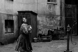 A black and white screen capture from The Girl with the Needle. It shows a girl in an alley way looking up and over her shoulder as if something was following her from above.