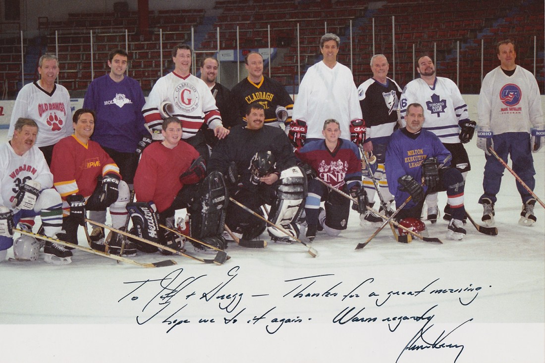 A group of hockey players pose on the ice at Matthews Arena, including Greg Smith and his father, with 2004 presidential candidate John Kerry standing in the back row as the tallest player.