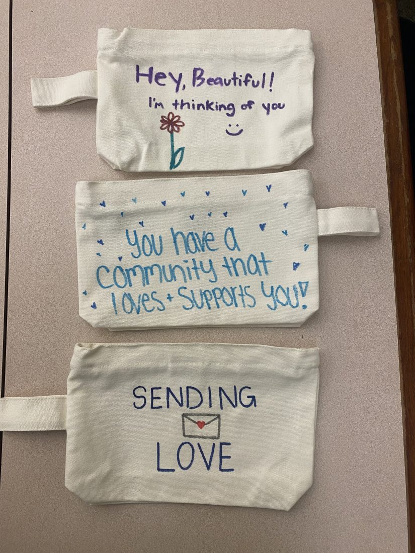 Three canvas pouches laid out on a table. One says 'hey beautiful! I'm thinking of you,' one says 'you have a community that loves + supports you,' and the last one says 'sending love' with an envelope drawn on it.