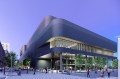 The exterior of a large multifloor athletic facility that is shaped in a rectangle with rounded edges. The sky behind it is purple.