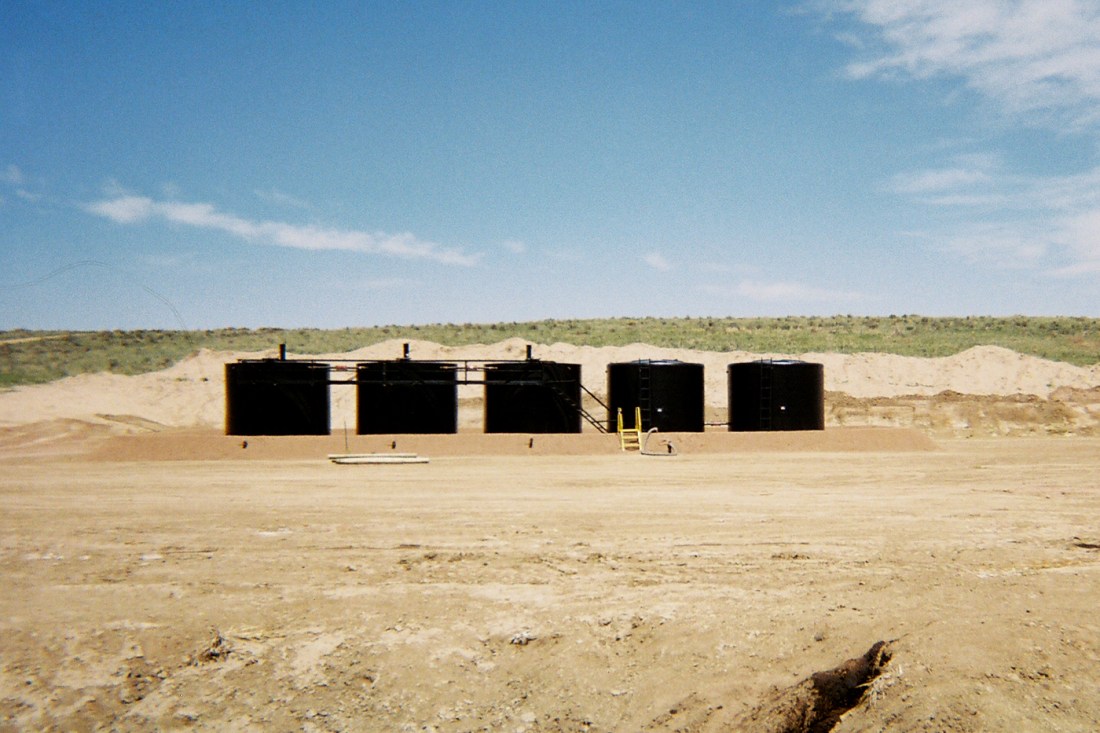 Five large black objects in a sandy field. 