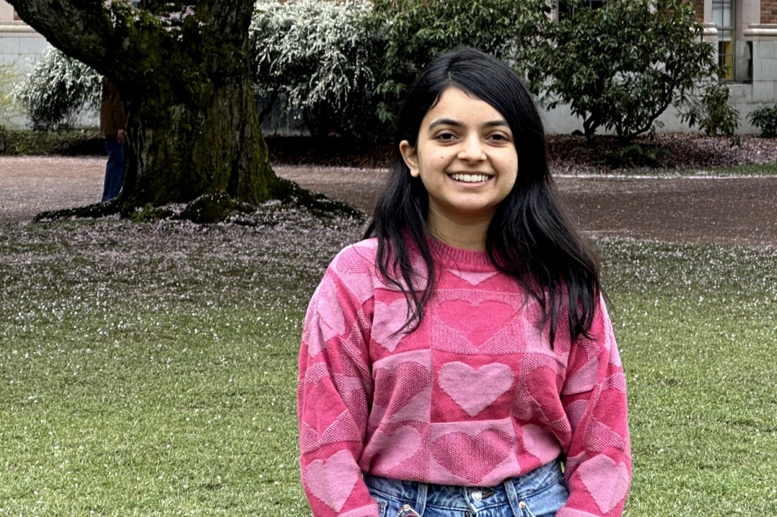 Portrait of Purvakshi Thakkar standing outside wearing jeans and a pink sweatshirt with hearts on it.