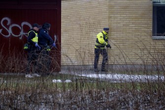 Two police officers outside of Risbergska School standing up against the wall with their guns drawn.