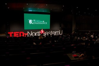 A person standing on stage in front of a sign that says 'TEDxNortheasternU'.