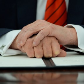 Donald Trump resting his arms folded on an executive order on a desk.