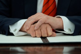 Donald Trump resting his arms folded on an executive order on a desk.