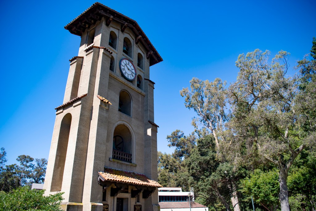 A bell tower outside in California with trees growing next to it.