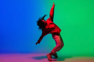A person dancing with their arms up and leaning backwards on a blue and green background.