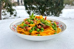 A bowl of pasta with peas and pancetta in it.