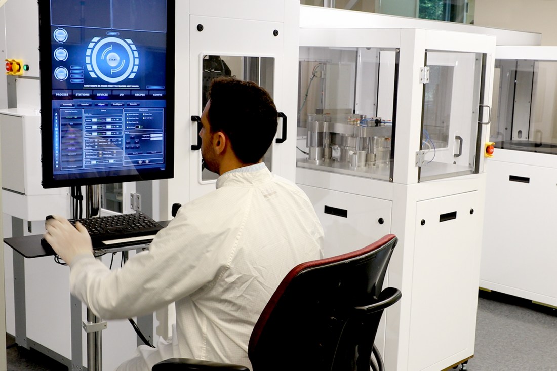 Ahmed Hafez Abdelaziz wearing a white lab coat and white gloves sitting at a printer.