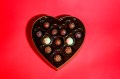 A heart shaped box of chocolates on a red background.