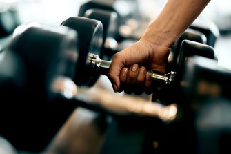 A hand picking up weights from a weight rack.