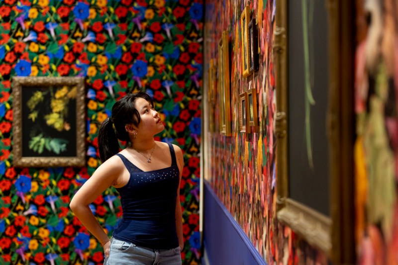 A person observes framed artwork on a vividly patterned wall in an exhibition space.