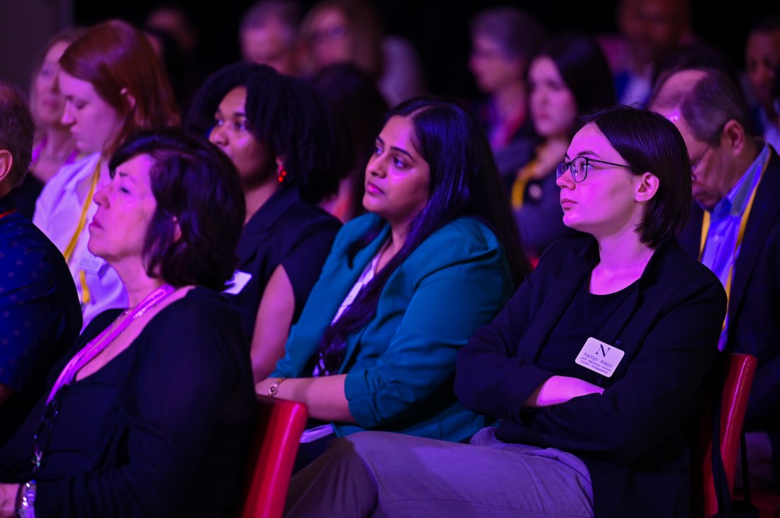 Audience members sitting in rows in a room lit with purple lighting.