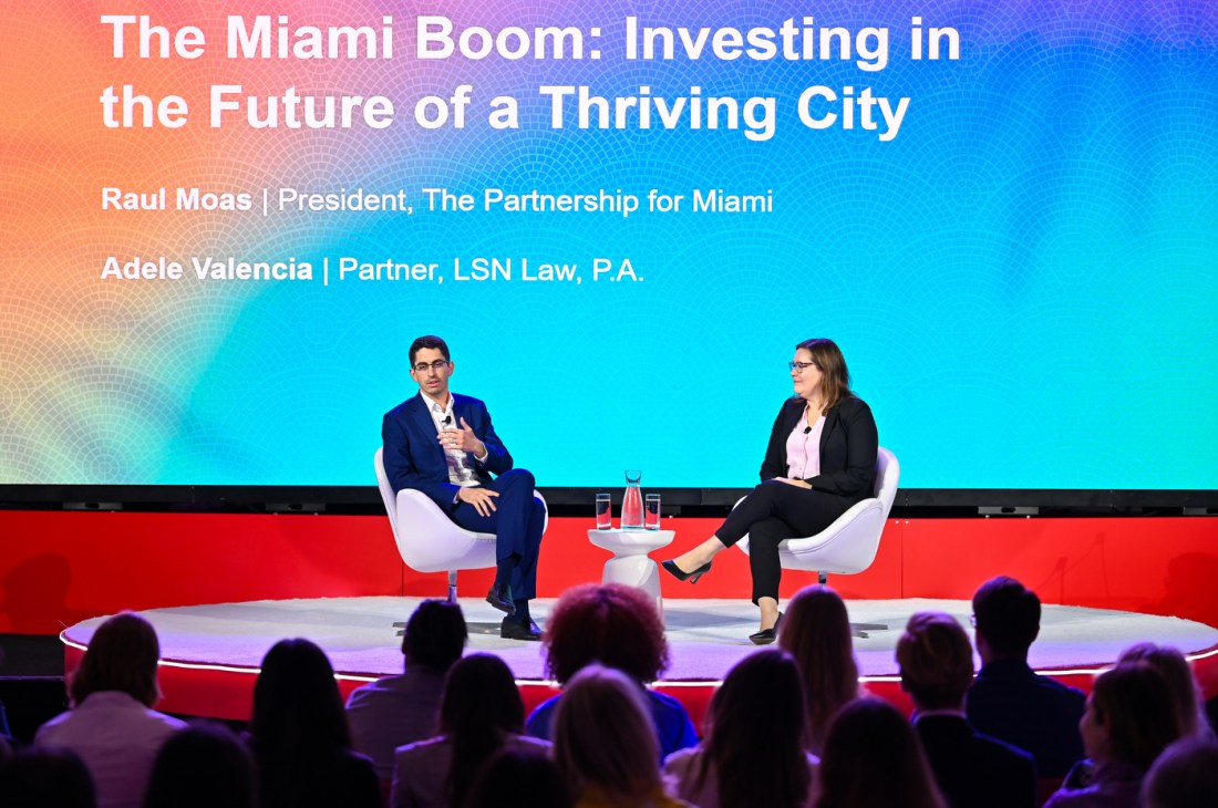 Raul Moas and Adele Valencia sitting across from each other on stage in white chairs. 