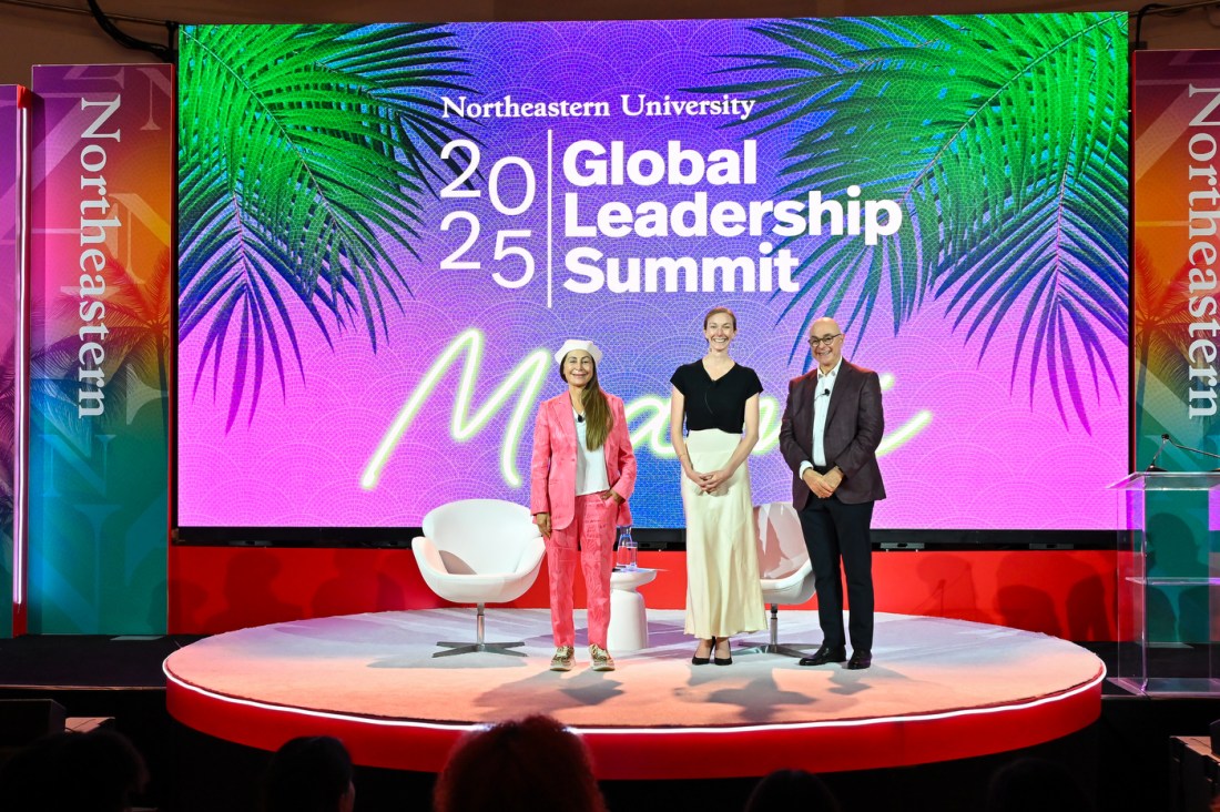 Northeastern President Aoun posing with two other people on stage in front of a screen that says 'Northeastern University 2025 Global Leadership Summit'.