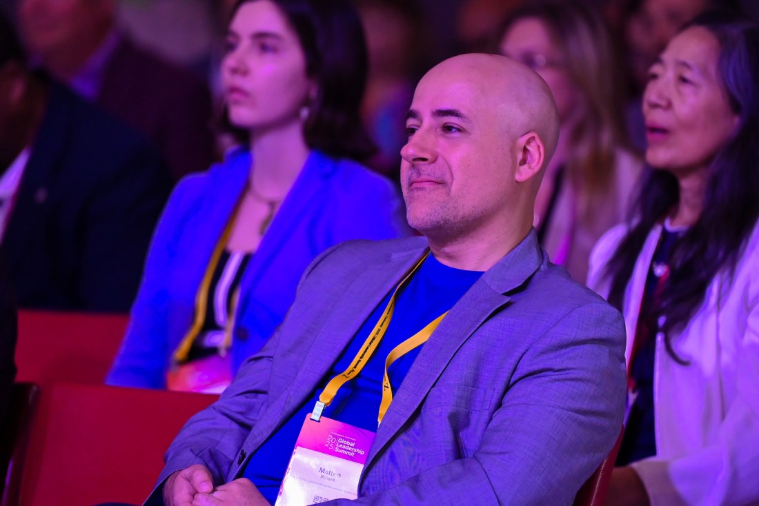 An audience member wearing a name tag on an orange lanyard listening from the audience.