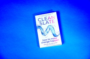 Kristen Lee's book 'Clean Slate' resting on a blue background. The cover of the book is white with the title on it in an all caps font that starts in blue on the left side of the cover and gradually transitions to pink on the right side.