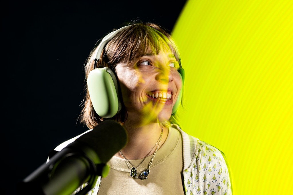 Adina Gitomer smiling as she sits in front of a microphone while wearing over the ear headphones.