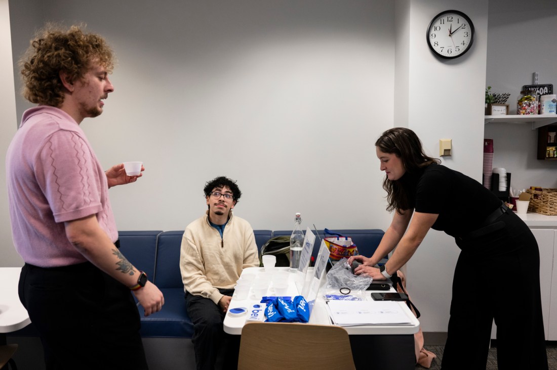 Matthew Chavez Cruz and two other people standing around a table with Bevi swag on it. On eof the people has a small cup that they are taste testing Bevi flavors from.