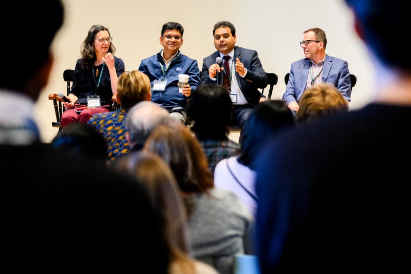 People participate in a panel discussion at an indoor event, with audience members listening attentively in the foreground.