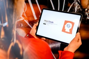 A person holding up a tablet open to the Claude AI web page.