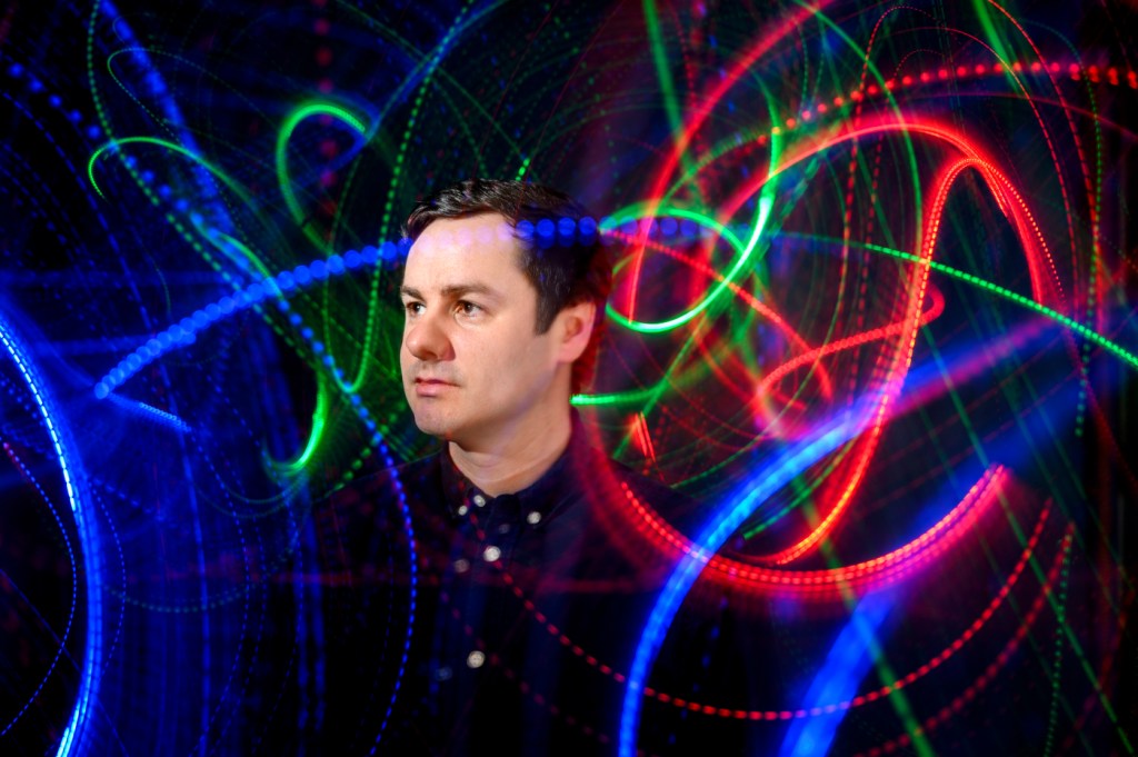 A person poses with colorful light trails in the background.