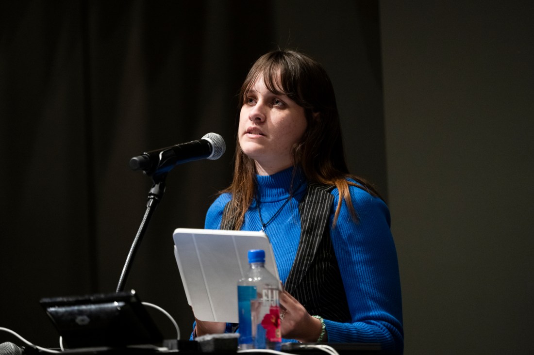 Meg Cassidy wearing a blue shirt speaking into a microphone while holding an iPad.