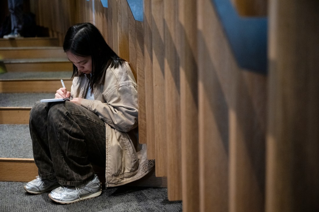 A student sitting on the stairs of the auditorium writing in a notebook.