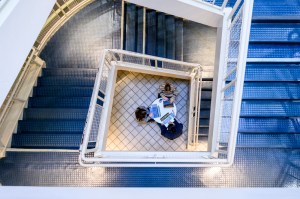 A group of people sit around a table working together, viewed from above through a staircase with blue steps.