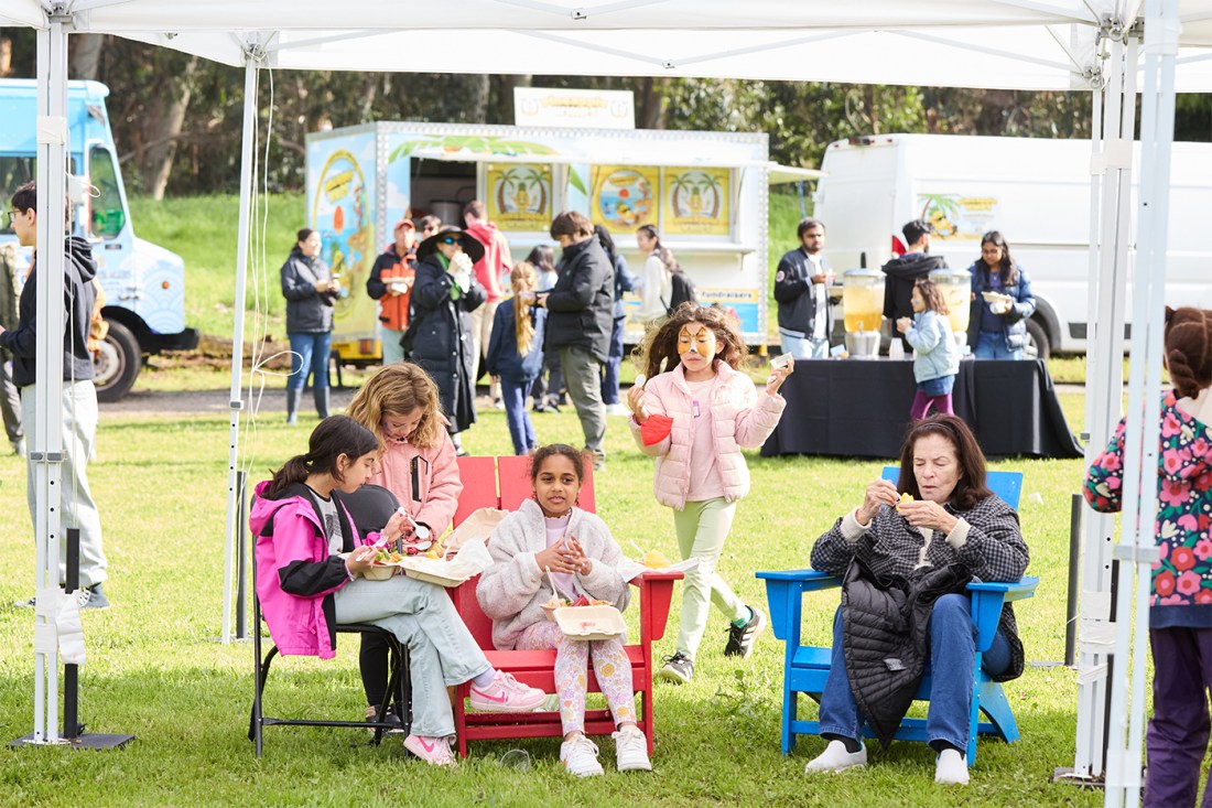 People sitting in lawn chairs underneath a white tent on the Oakland Campus.