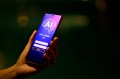 A person's hand holding a smartphone open to a purple screen that says 'AI' on it over a graphic of the human brain.