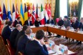 World leaders sitting around a square shaped table at a summit. Next to the table are a series of flags representing the countries that the leaders represent.