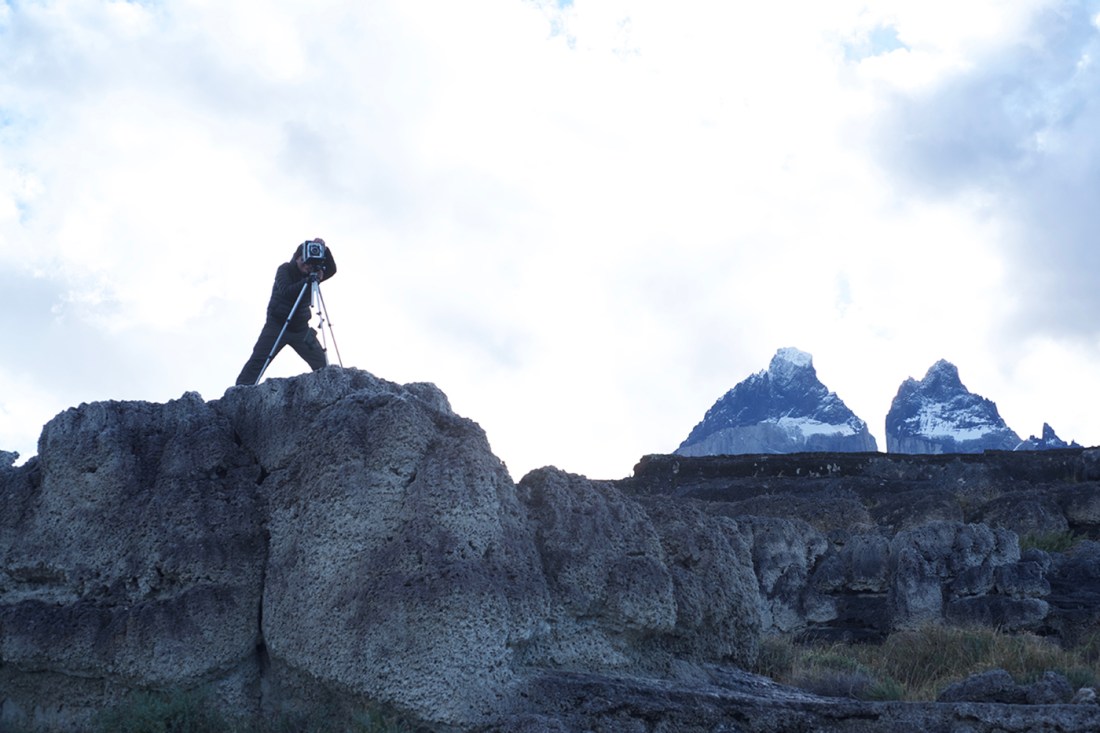 Someone stands on a cliff taking a photo with a tripod.