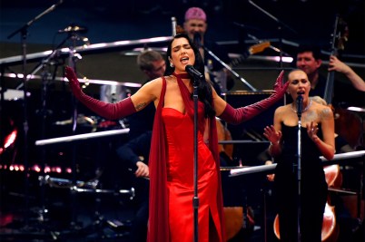 Dua Lipa wearing a red dress while singing into a microphone at the Royal Albert Hall.