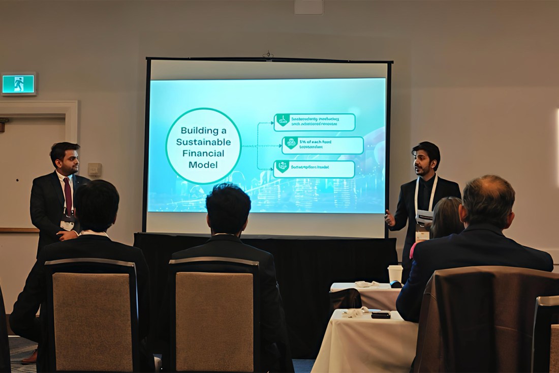 Two students standing on either side of a projector screen that has a slide on it with the title 'Building a Sustainable Financial Model'. 