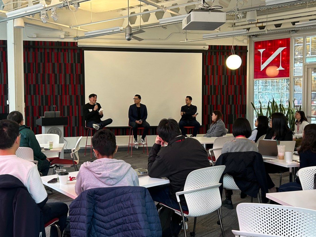 A panel of three people sitting at the front of a room of audience members.