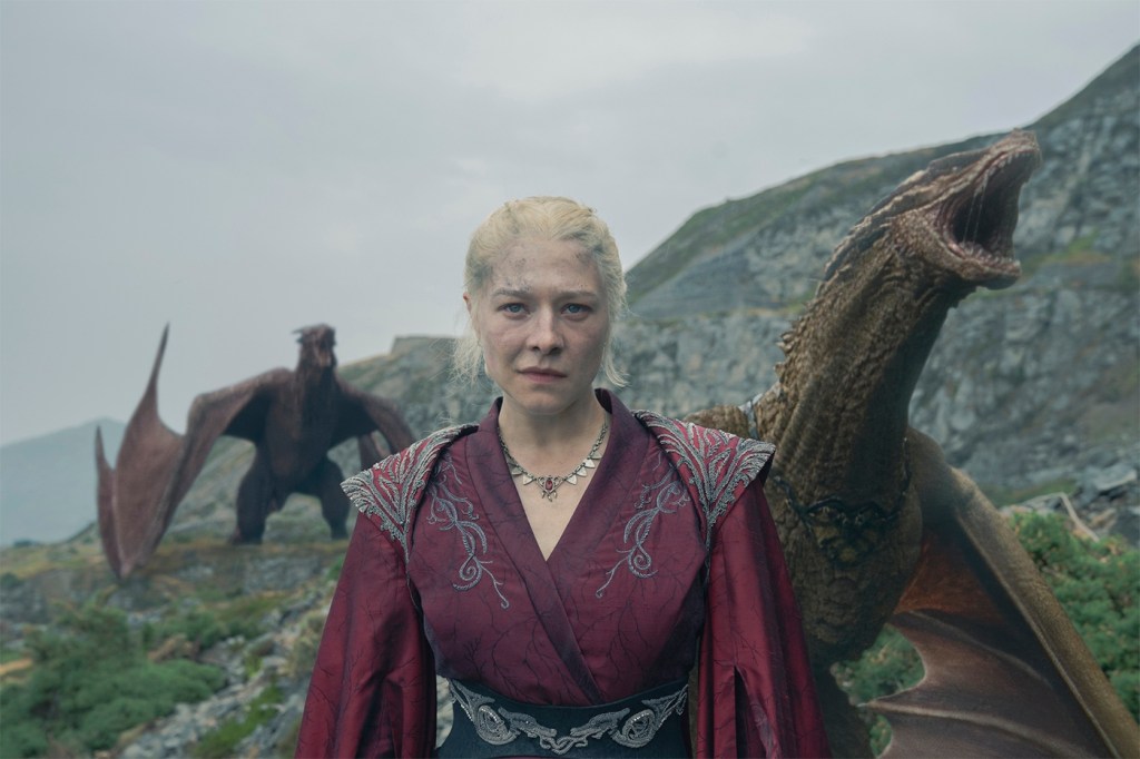 A screen capture from a scene of House of the Dragon. In it, a woman is standing in front of several dragons in a mountainous landscape.